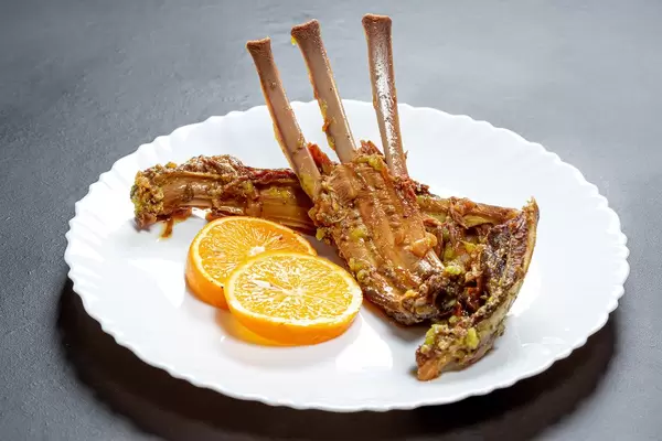 Baked ribs of young lamb with slices of fresh orange in a plate on a black background