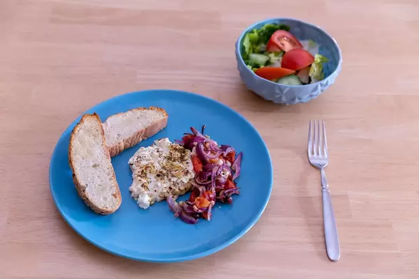 Baked shepherds cheese with tomatoes-onion stew and garlic bread on a blue plate and a fresh mixed salat