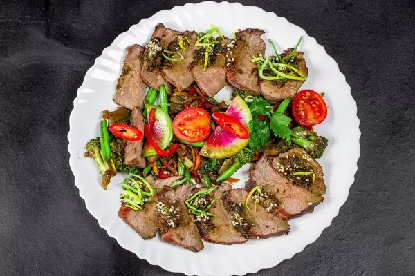 Baked vegetables with beef slices on a black background, top view (Flip 2020)