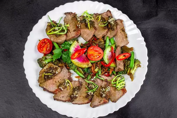 Baked vegetables with beef slices on a black background, top view