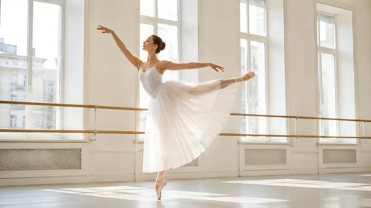 Ballerina in weißem Kleid tanzt im hellen Ballettsaal