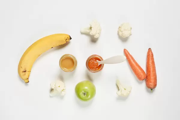 Banana and carrot-based purees with apple fruit and broccoli on white