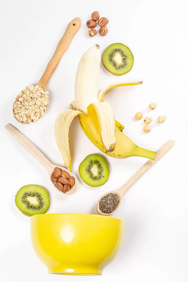 Banana, kiwi, nuts, chia seeds and oatmeal with yellow bowl, top view