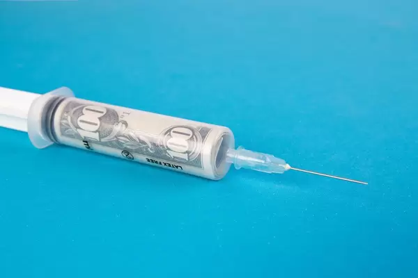 Banknote of $100 inside a syringe for injections on blue background