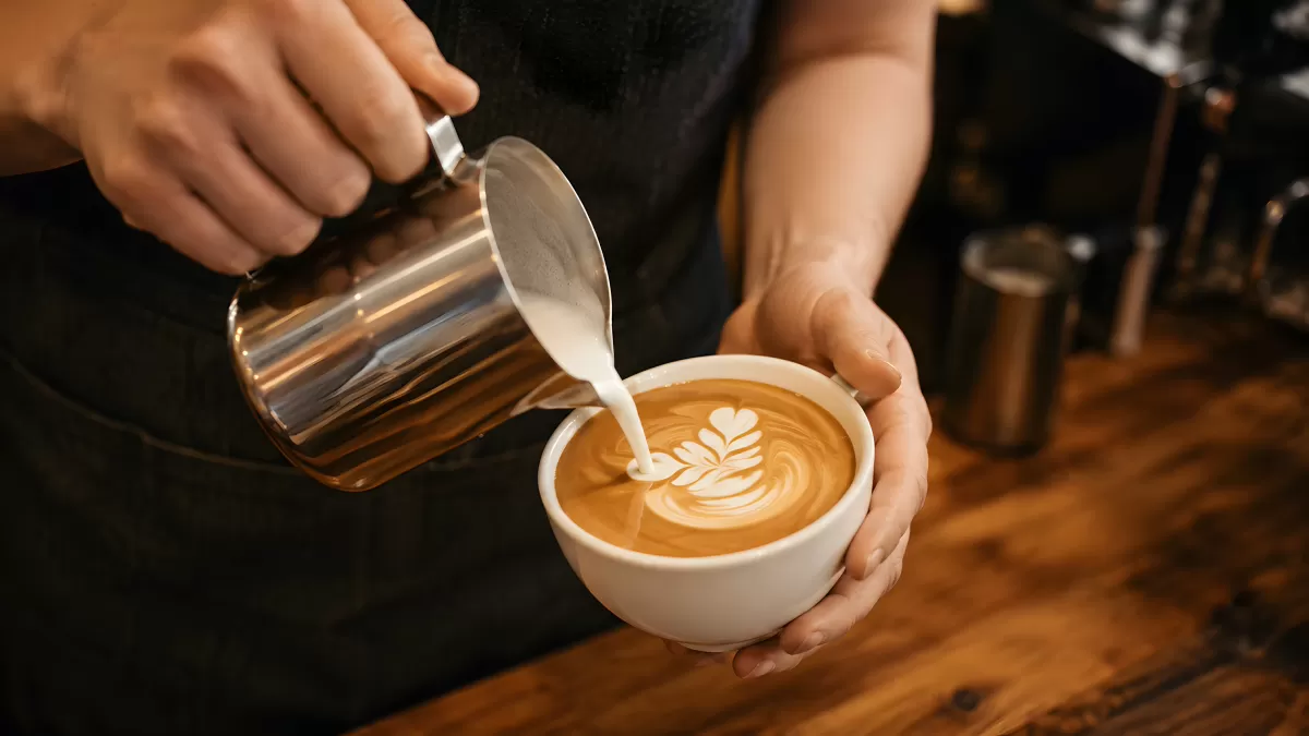 Barista gießt Milchschaum für Latte Art in Tasse