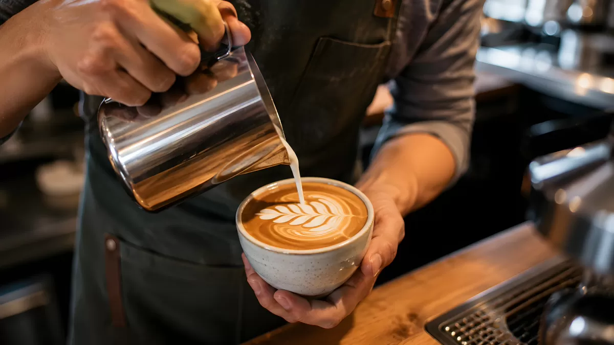 Barista gießt Milchschaum-Latte-Art in Keramiktasse