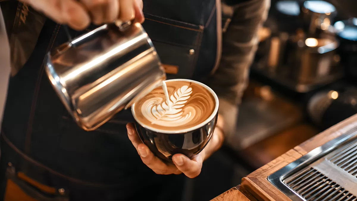 Barista gießt Milchschaum-Rosette in Cappuccino