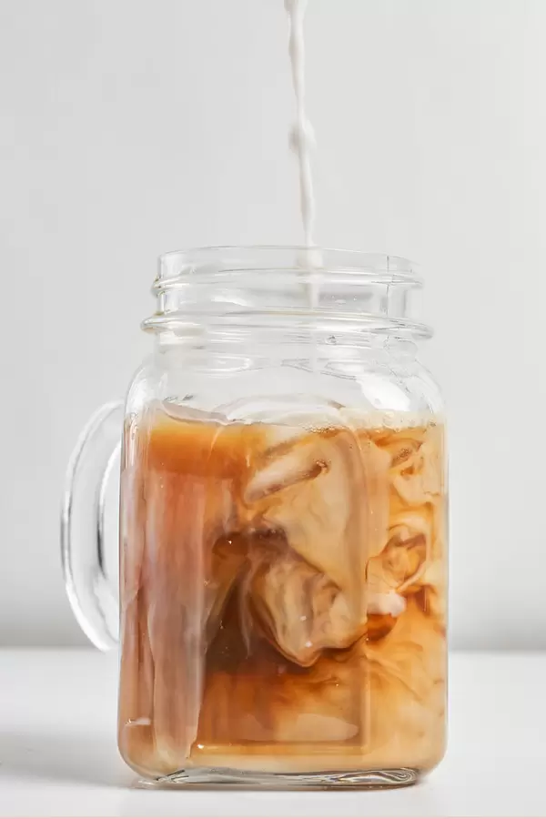 Barista pouring milk Into a glass of iced coffee