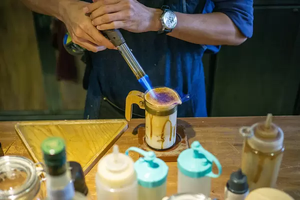 Barista preparing a Dalgona Coffee and using a Gas Burner to caramelize Sugar in a Coffee Shop