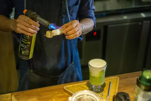 Barista uses Bunsen Gas Burner to torch Marshmallow on a Skewer with Cookies to decorate Milk Coffee