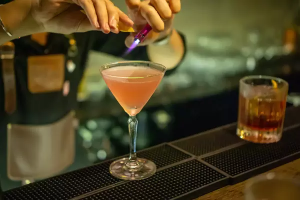 Bartender using a Storm Lighter to burn Lemon Drops to prepare a Cocktail in a Martini Glass