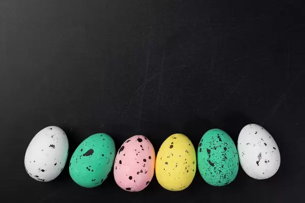 Basis für Grußkarte zu Ostern mit in Linie aufgereihten bunten Ostereiern auf schwarzem Hintergrund