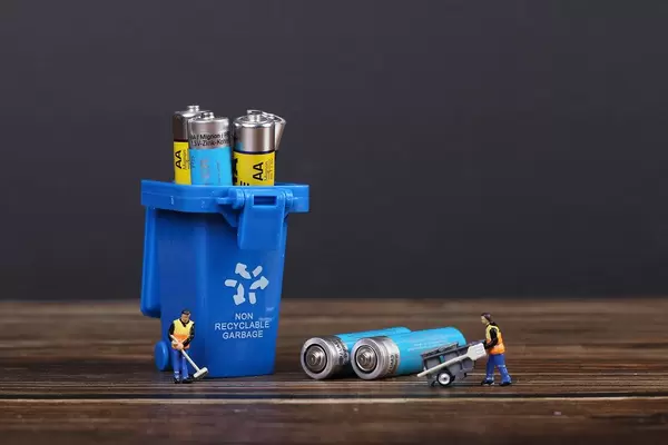 Batteries in blue recycle bin with tiny cleaning workers