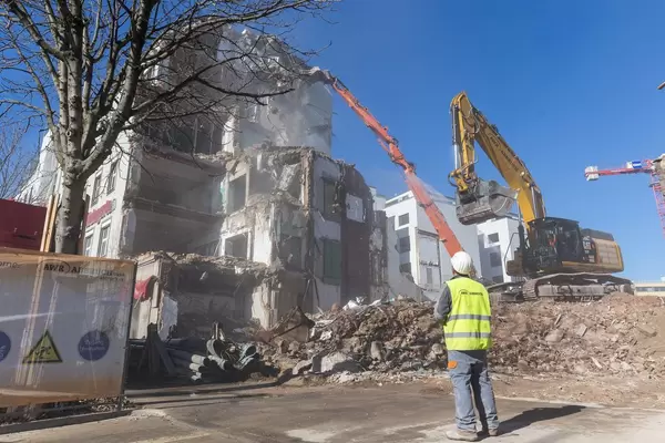 Bauarbeiter beaufsichtigt Hausabriss mit Kran und Bagger