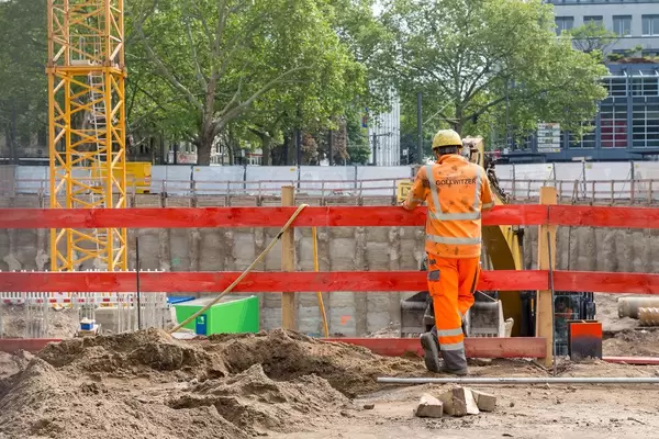 Bauarbeiter mit Helm beobachtet seinen Kollegen im Bagger auf dem Rudolfplatz in Köln