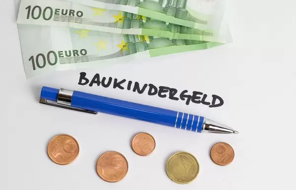 Baukindergeld - Schriftzug mit Kugelschreiber, Geldscheinen und Münzen