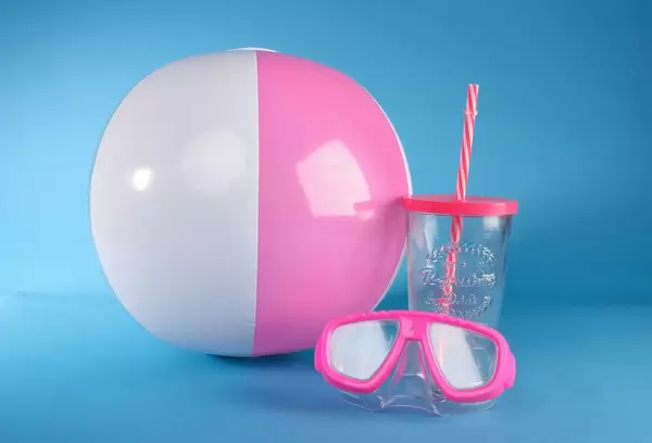 Beach ball with diving mask and drinking glass on blue background