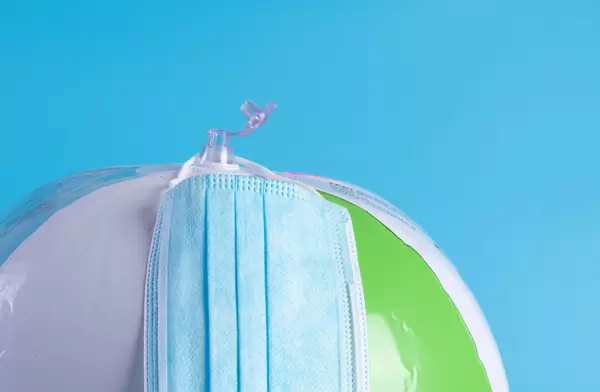 Beach ball with medical face mask on blue background