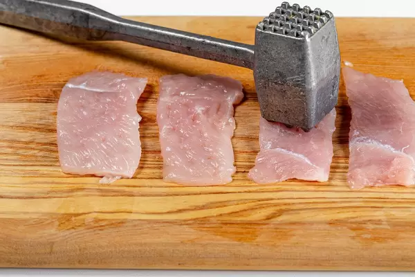 Beating chicken fillet with a kitchen hammer