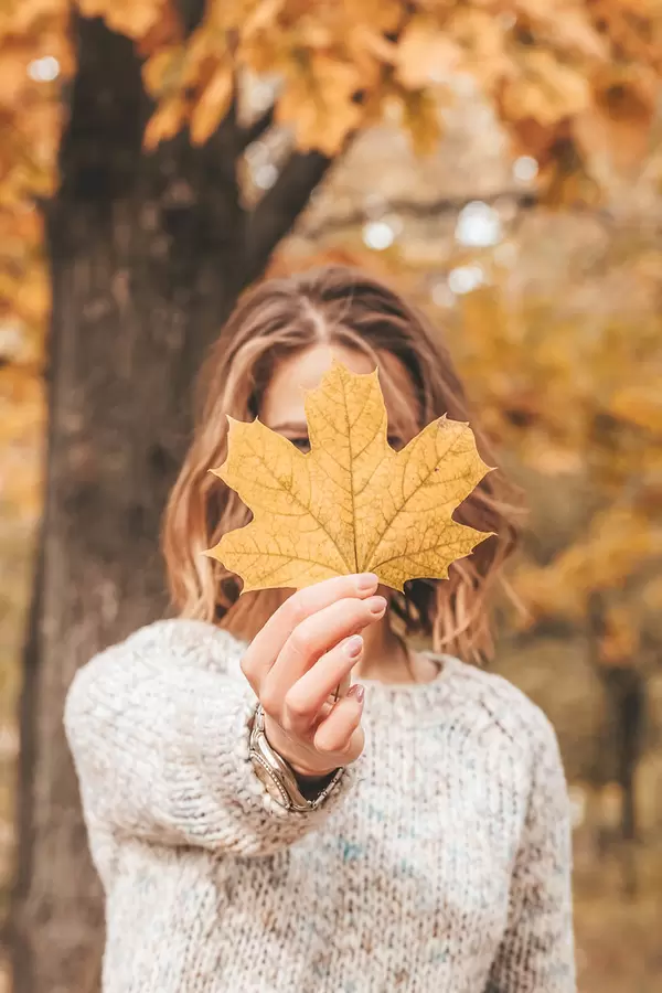 Beautiful autumn portrait of woman with maple leaf in hand