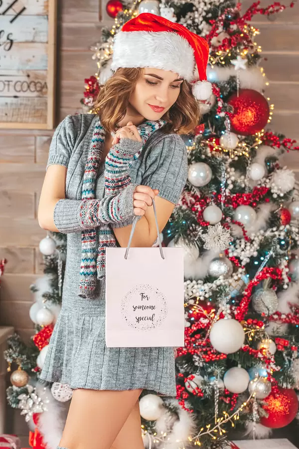 Beautiful girl in a knitted dress and santa hat with a gift bag in her hands