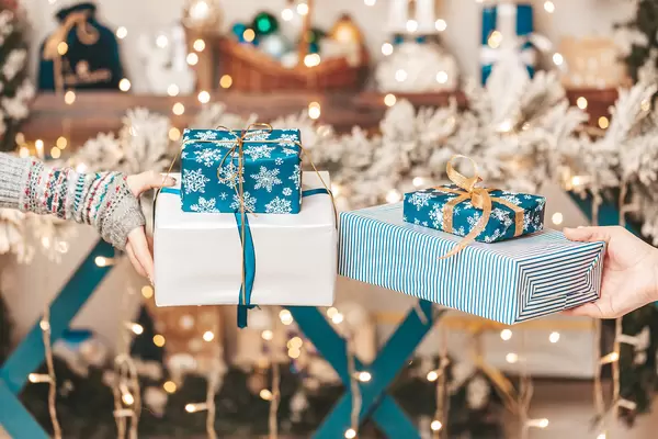 Beautiful holiday gifts in female hands on a blurred background of garlands in the christmas room