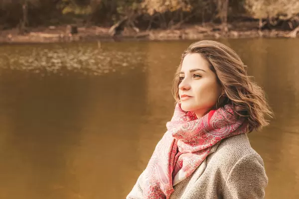 Beautiful pensive girl near the autumn pond