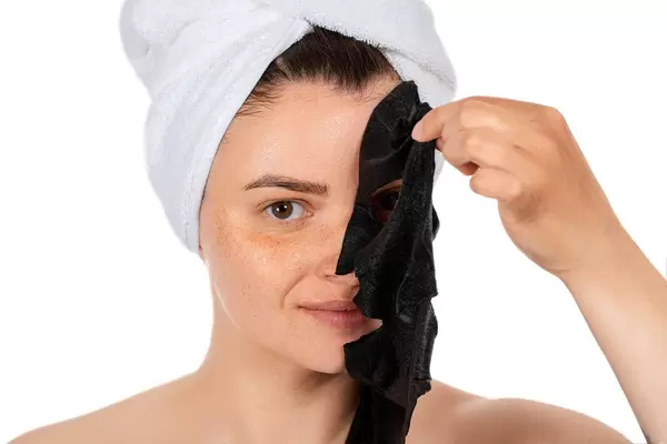 Beautiful woman is removing purifying mask from her face over white background