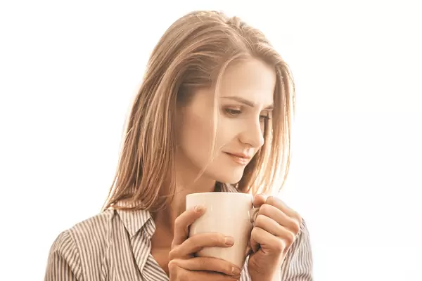 Beautiful woman with cup of tea standing near window