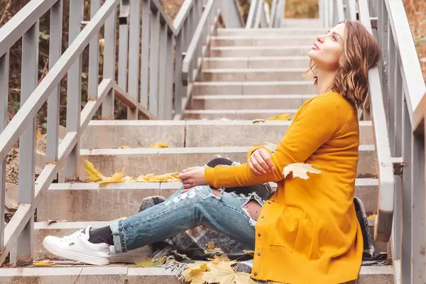 Beautiful young woman sitting on the steps with a yellow maple leaf in her hand