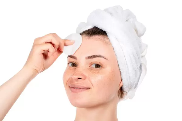 Beautiful young woman with freckles on her face and cotton pad in her hand on a white background