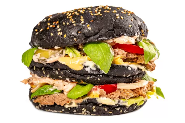 Beef burger with a black bun, lettuce,basil, sauce and vegetables