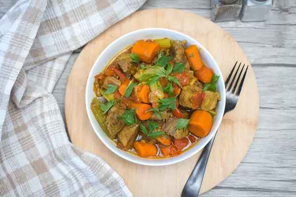 Beef stew with carrots, apio, paprika and parsley in a bowl on a round wooden board - top view