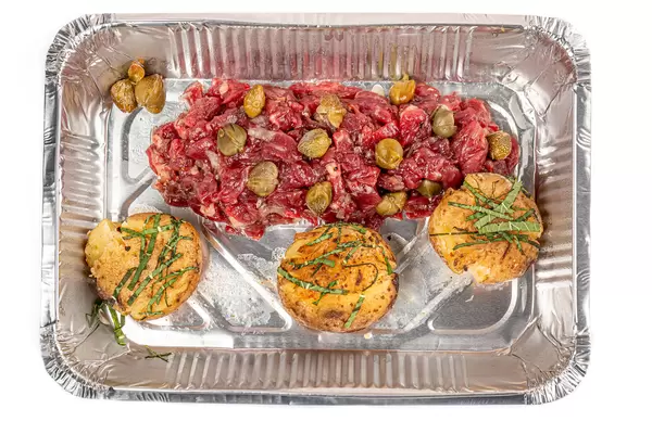 Beef tartare with potatoes and capers in a container, top view