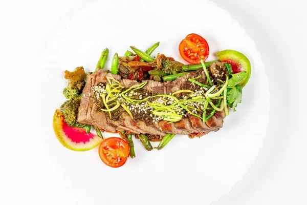 Beef tenderloin with vegetables and spicy sauce on a white plate, top view (Flip 2020)