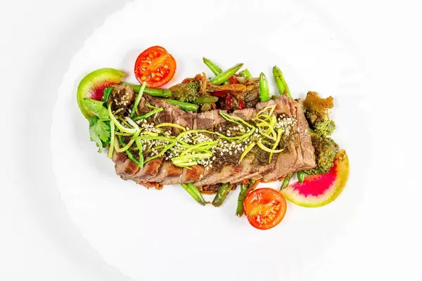 Beef tenderloin with vegetables and spicy sauce on a white plate, top view