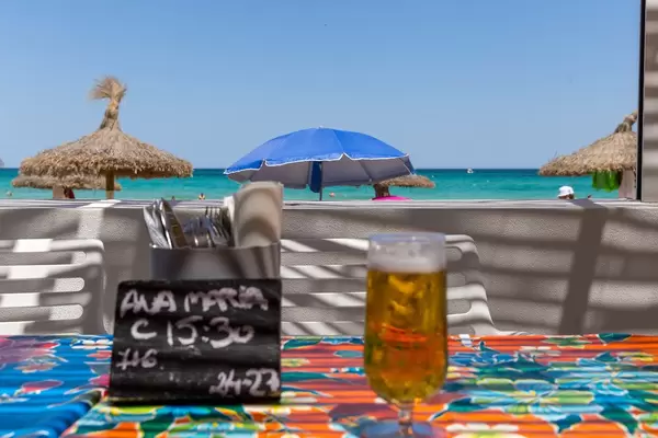Beer by the sea. Draught beer, reservation card and cutlery with beach umbrellas in the background