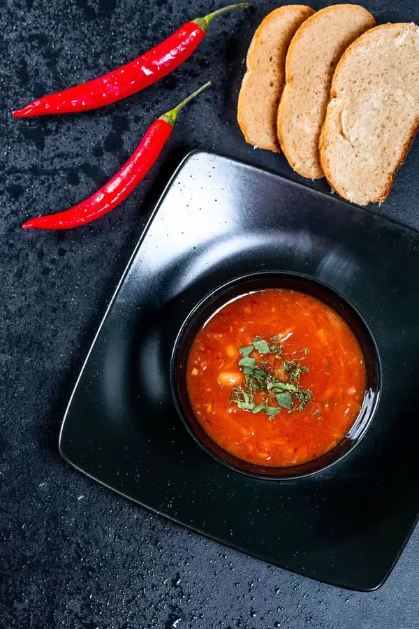 Beetroot tomato soup with slices of bread and chili on a black background