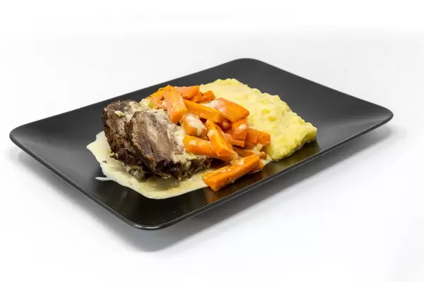 bei Lieferdienst bestellter Tafelspitz mit gedämpften Karotten, Kartoffelpüree und Soße auf schwarzem Teller