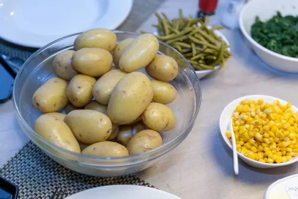 Beilagen zu Raclette wie Pellkartoffeln, Maiskörner, Bohnen und Spinat in verschiedenen  Schüsseln