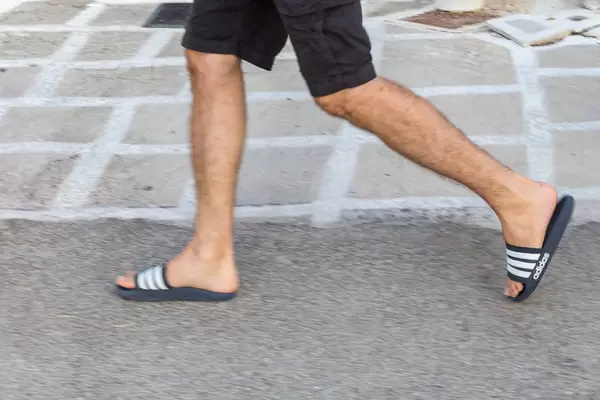 Beine eines Mann in Shorts und Adiletten der über Pflastersteine geht