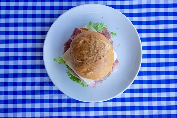 Belegtes Brötchen mit Schinken, Käse, Tomaten, Gurken, Salat und Remoulade auf einem Teller von oben fotografiert