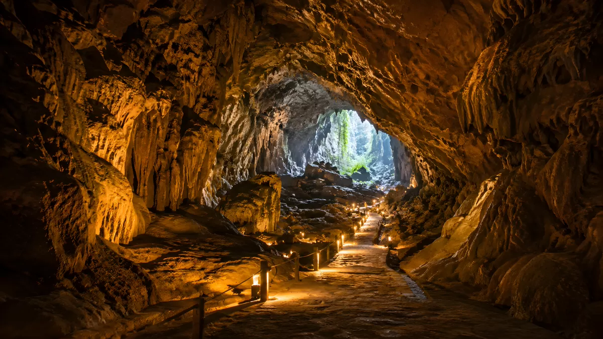 Beleuchteter Höhlenweg mit Stalaktiten und Tageslicht