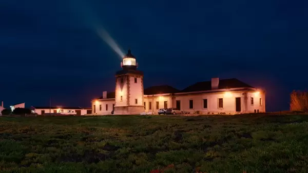 Beleuchteter Leuchtturm bei Nacht strahlt Lichtkegel in Himmel bei Carrapateira, Portugal