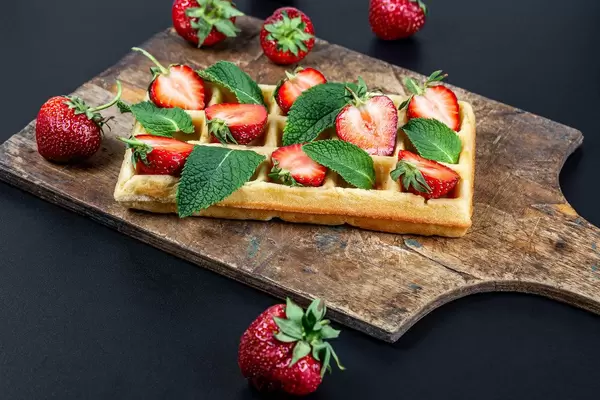 Belgian waffle with sliced strawberries and mint leaves on an old kitchen board