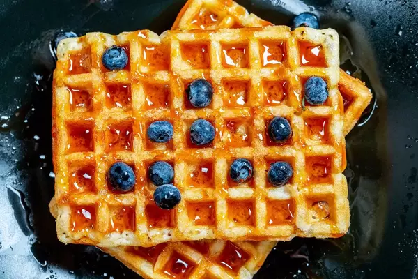 Belgian waffles poured with honey and blueberries. Top view (Flip 2019)