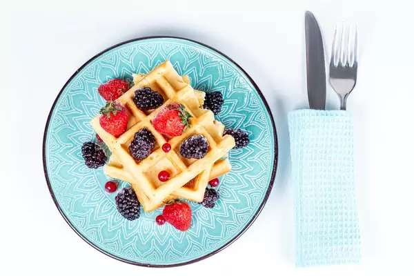 Belgian waffles with berries in a plate on white, top view