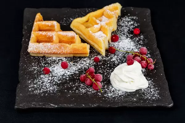Belgian waffles with red currant, powdered sugar and whipped cream on a black background