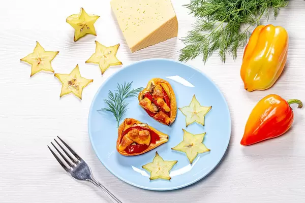 Bell pepper halves baked with tomatoes and cheese on a white wooden background with slices of fresh carambola and dill (Flip 2019)