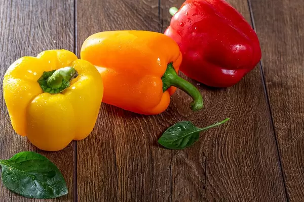 Bell pepper with green leaves on a brown wooden background